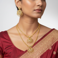 Gold-plated CZ necklace set with peacock chand pendant and matching studs, flat-lay on white with green plant