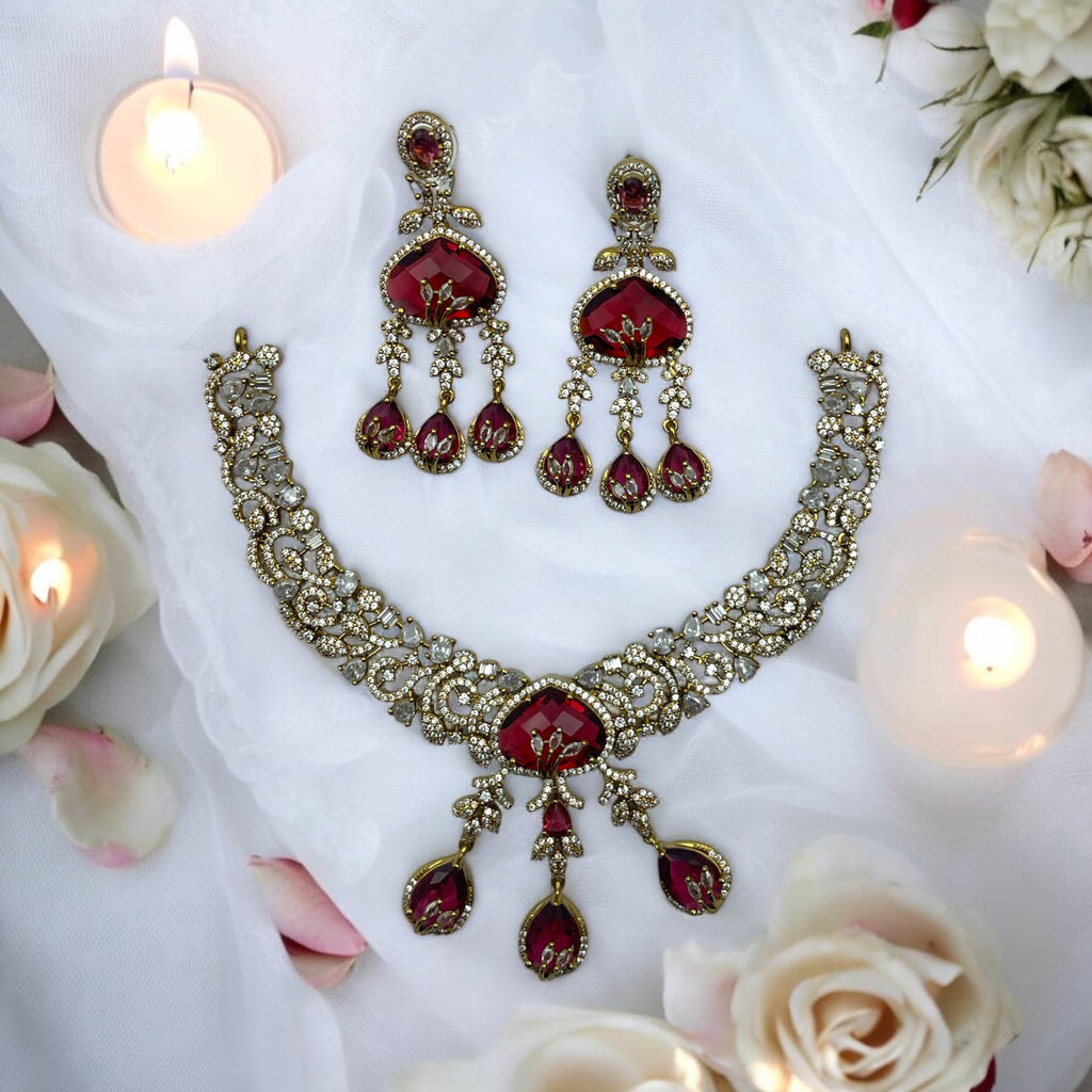 Antique gold necklace and earrings set with red gemstone drops, festive flat-lay with candles and roses