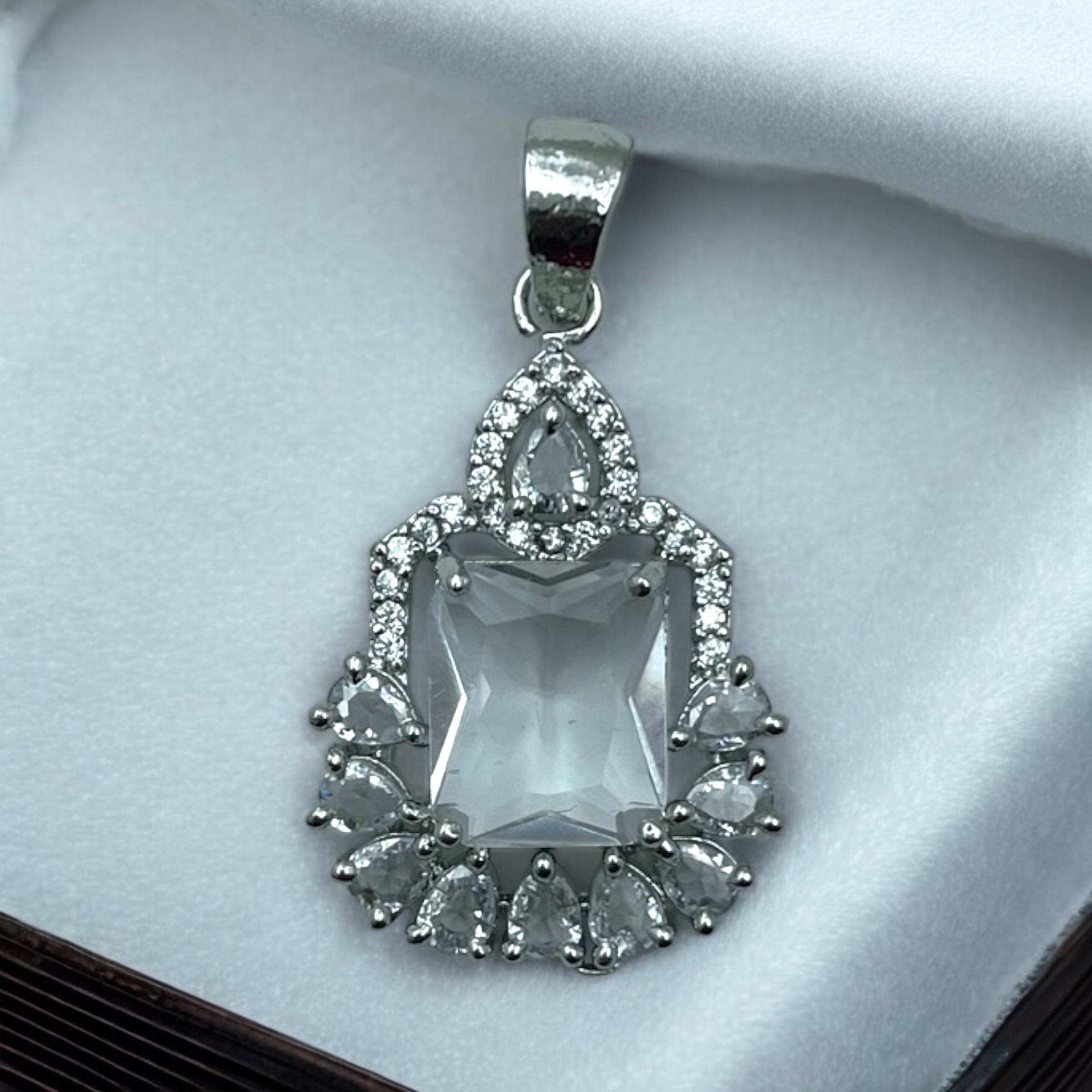 Silver-tone emerald-cut crystal pendant with pear and round CZ teardrop halo, flat-lay close-up