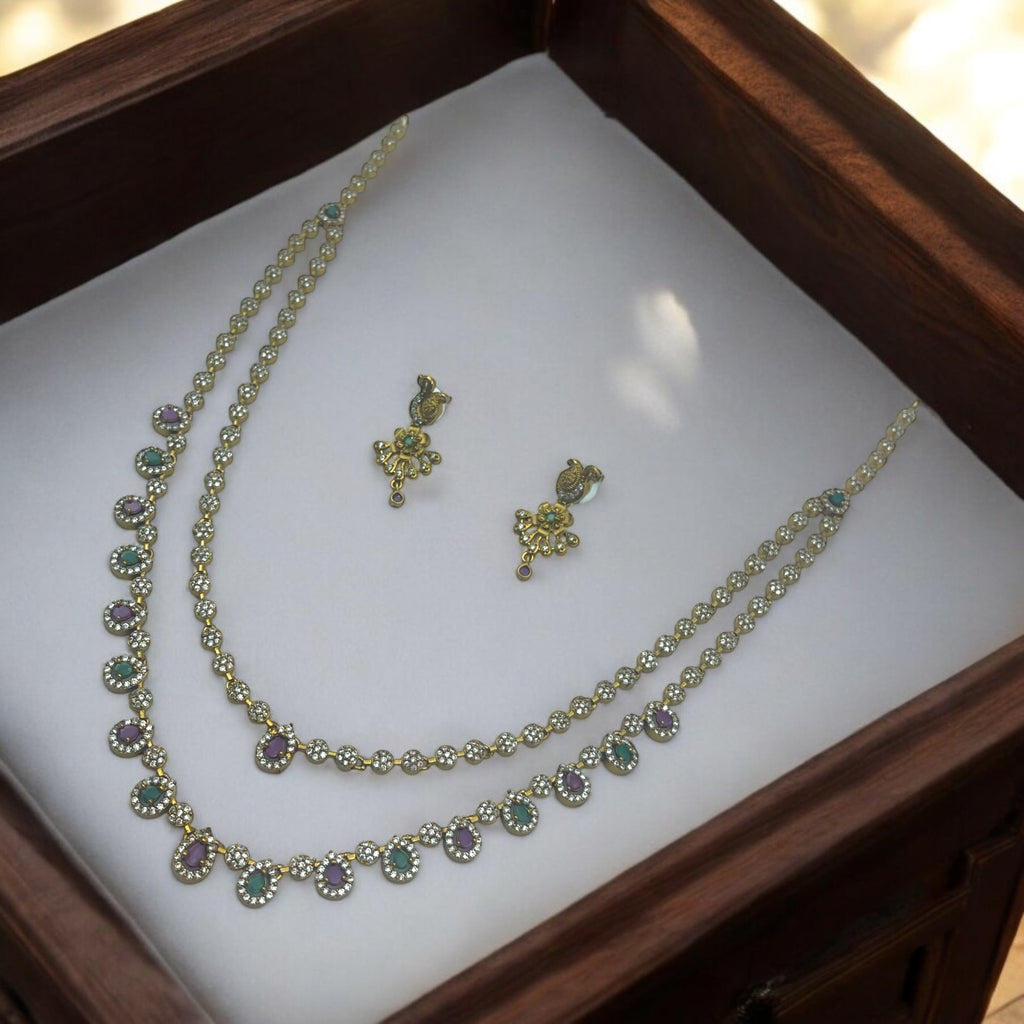 Antique gold two-layer stone necklace set with floral stud earrings, close-up flat-lay showing green and purple halo stones