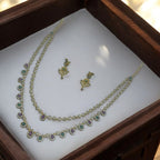 Antique gold two-layer stone necklace set with floral stud earrings, close-up flat-lay showing green and purple halo stones