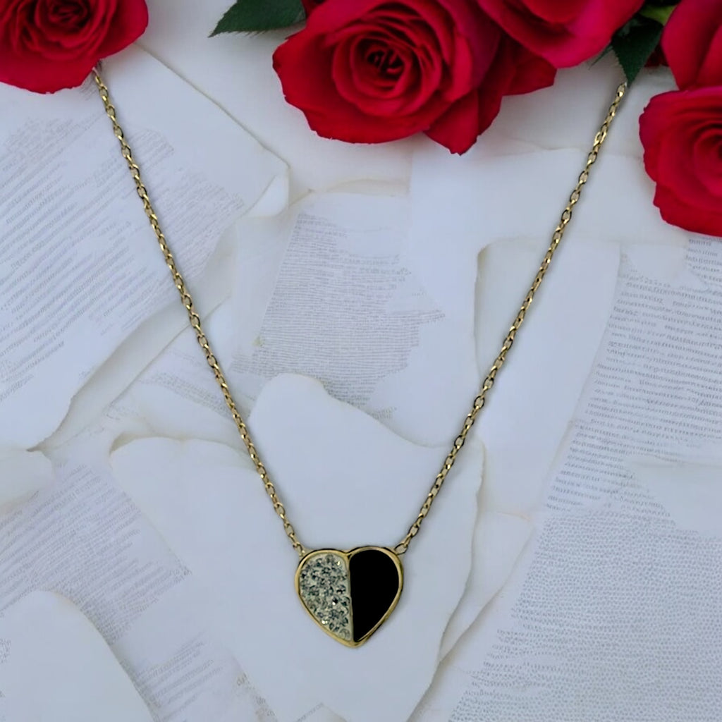 Gold-toned half-heart pendant necklace with pave crystal and black halves, flat-lay with roses