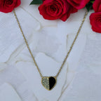 Gold-toned half-heart pendant necklace with pave crystal and black halves, flat-lay with roses