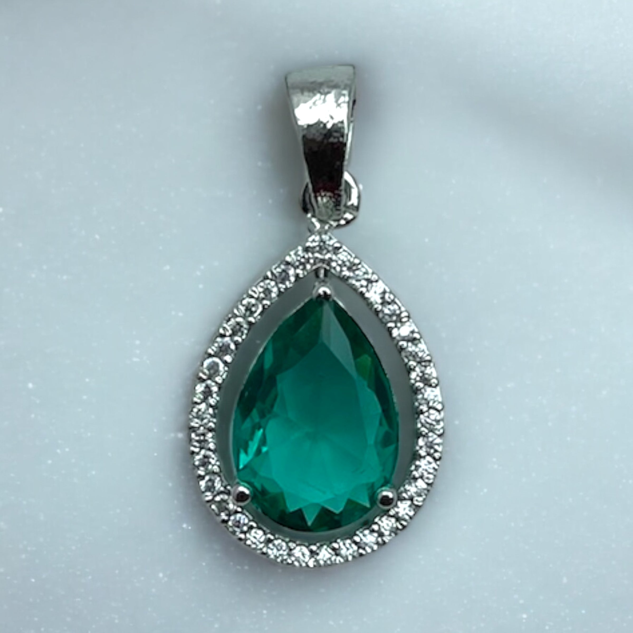 Silver-tone pear emerald pendant with clear stone halo, flat-lay close-up