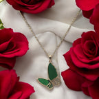 Gold-toned green butterfly pendant necklace with crystal accents, flat-lay with red roses