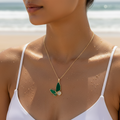 Gold-toned green butterfly pendant necklace with crystal accents, worn on model at the beach