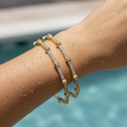 Gold-plated CZ pave bangles with floral accents, worn on wrist poolside showing waterproof shine