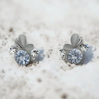 Silver-tone dewdrop crystal stud earrings with petal accents, pair flat-lay on textured white surface