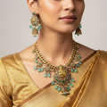Gold Lakshmi temple necklace set with green, ruby and pearl accents, worn on model with matching earrings