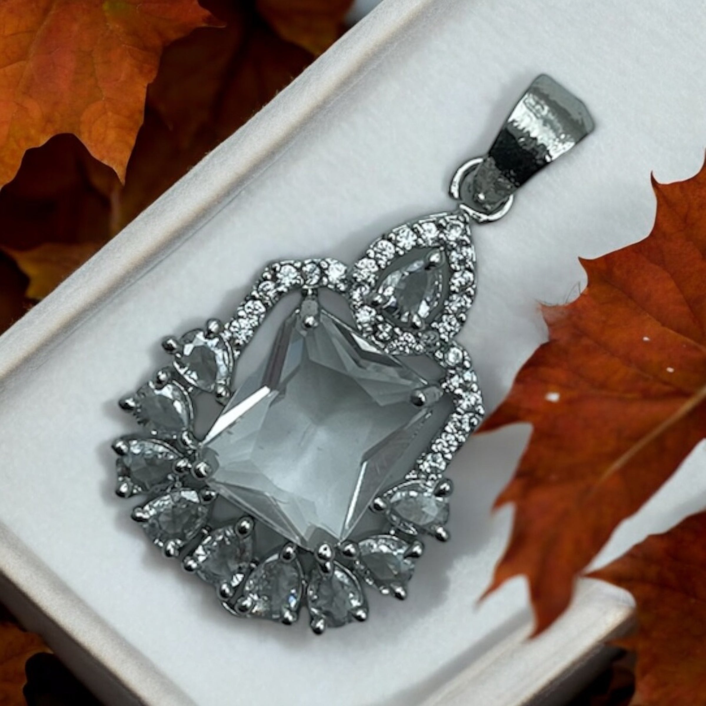 Silver-tone emerald-cut crystal pendant with pear CZ halo, worn on a woman's neck on a fine chain
