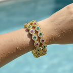 Gold-plated floral bangle set with American Diamond, ruby and emerald accents, worn on wrist by a pool