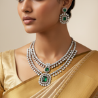 Silver-toned double-layered necklace set with white stones and emerald-green gems, flat-lay with candle and roses