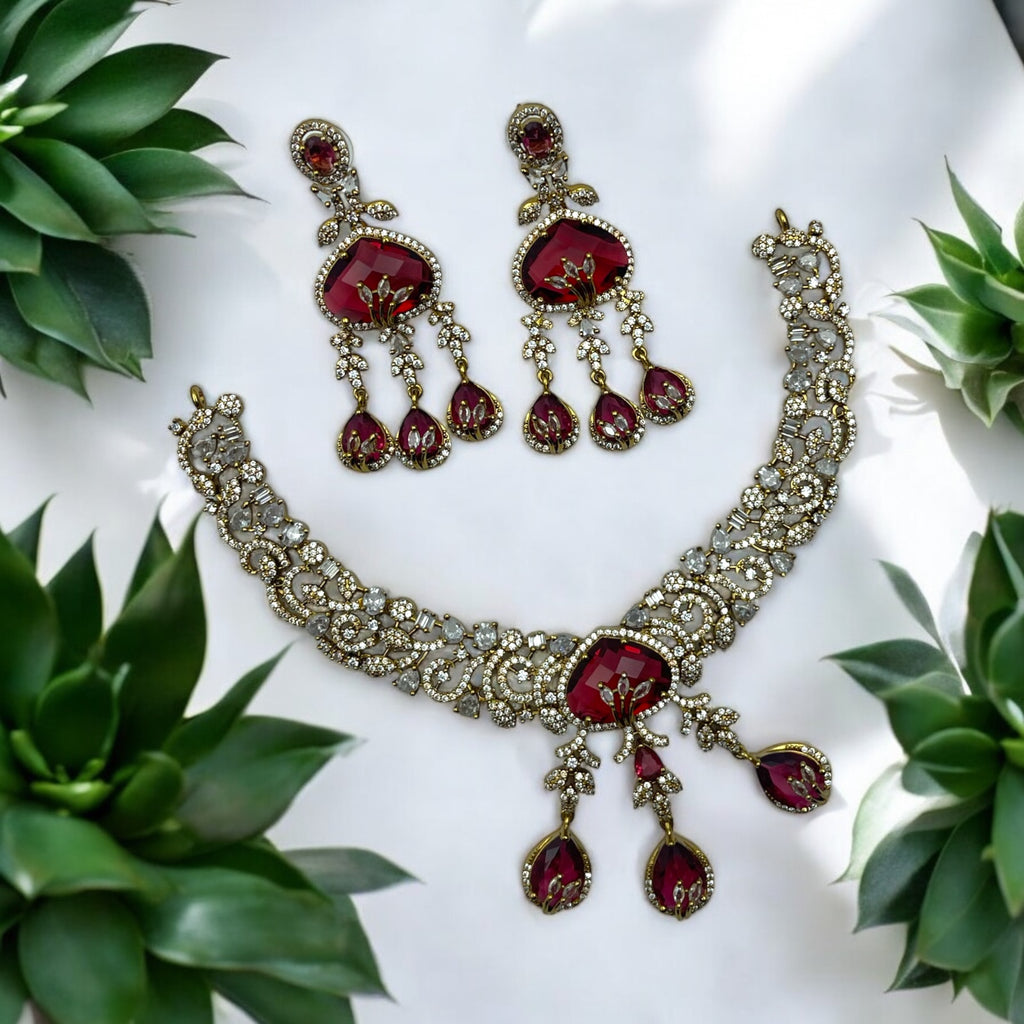Antique gold necklace set with red gemstone drops and sparkling stones, flat-lay with greenery