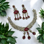Antique gold necklace set with red gemstone drops and sparkling stones, flat-lay with greenery