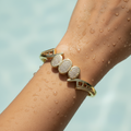 Gold-toned pave bangle bracelet with three sparkling oval charms, worn on wrist by pool
