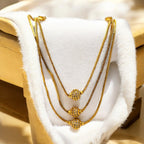 Gold layered necklace with three crystal-studded orbs, flat-lay draped on white fur