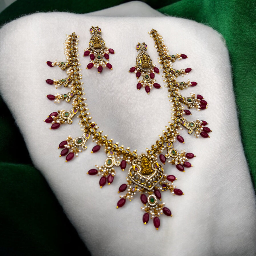 Gold-plated Lakshmi temple necklace set with ruby beads, white stones and pearl clusters, flat-lay close-up with matching earrings