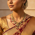Gold-plated Lakshmi temple necklace set with ruby beads, white stones and pearl clusters, flat-lay close-up with matching earrings