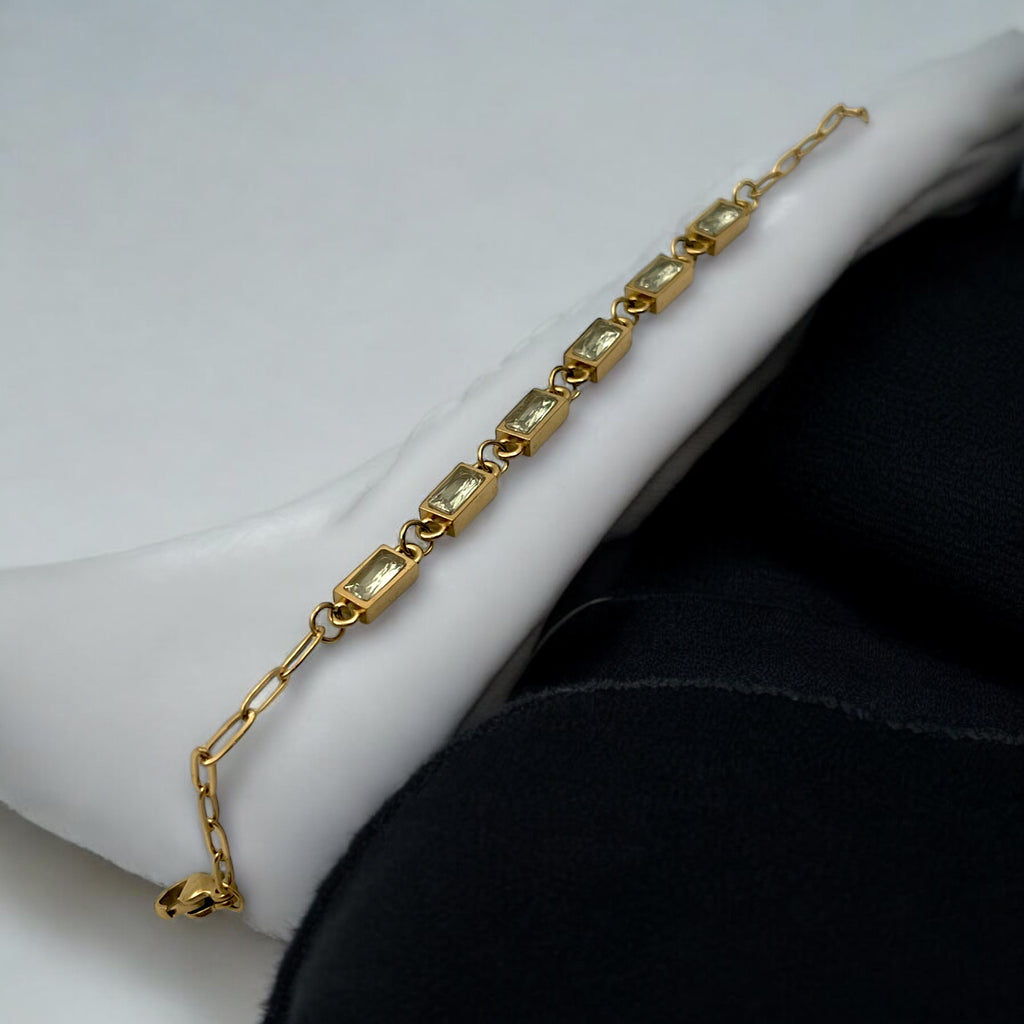 Gold-toned baguette chain bracelet with bezel-set clear stones, worn on wrist