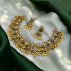 Antique gold Kundan necklace set with white stones and pearl cluster fringe, flat-lay with matching earrings on silk