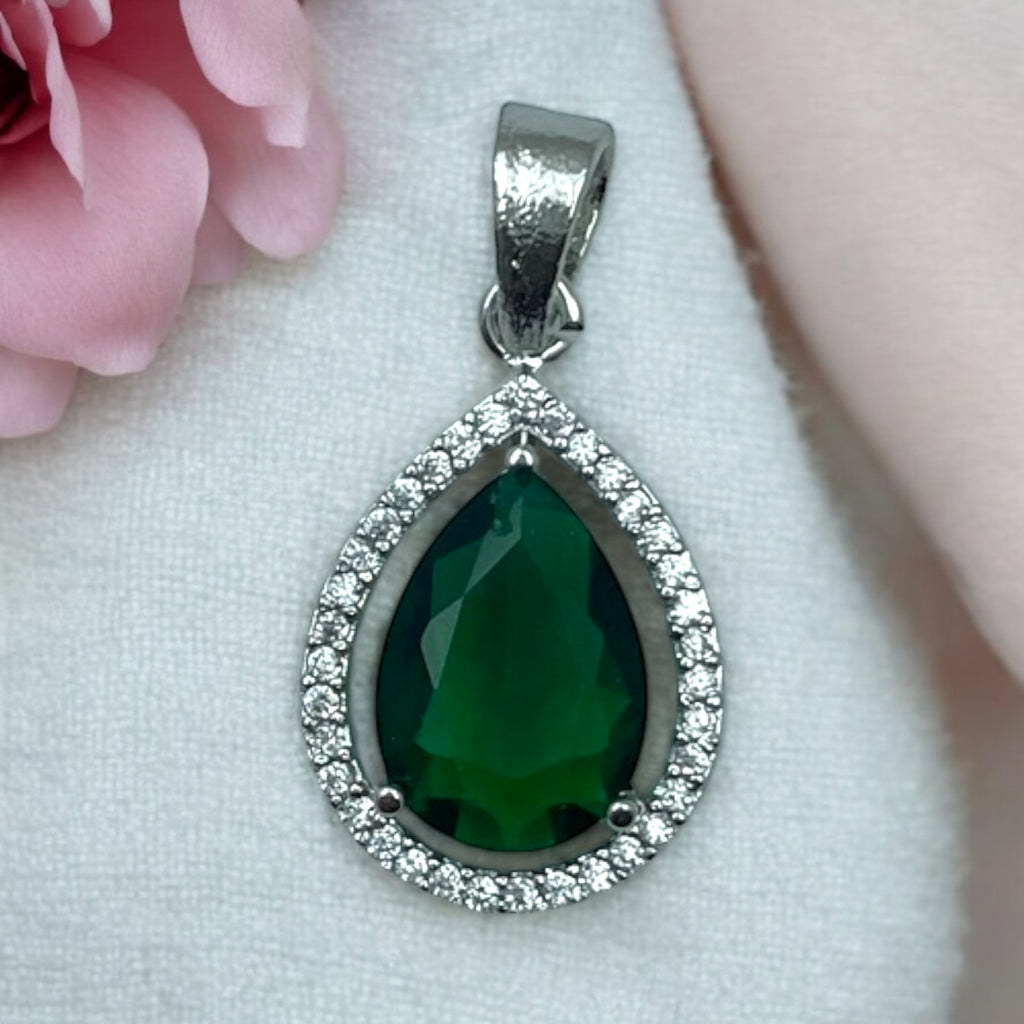 Silver-tone green pear pendant with clear-stone halo, flat-lay close-up on soft fabric