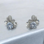 Silver-tone dewdrop crystal stud earrings with petal accents, pair flat-lay on marble surface
