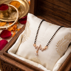 Gold-tone heartbeat mangalsutra with studded pendant and pearl drop, flat-lay in wooden jewelry box with rose petals