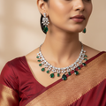 Silver-tone necklace set with emerald-green teardrop crystals and clear CZ florals, flat-lay with earrings on autumn leaves