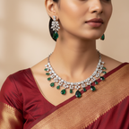 Silver-tone necklace set with emerald-green teardrop crystals and clear CZ florals, flat-lay with earrings on autumn leaves