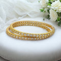 Gold-plated bangle set with princess-cut white CZ stones, flat-lay close-up on white roses