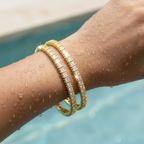 Gold-plated bangle set with princess-cut white CZ stones, flat-lay close-up on white roses