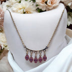 Gold-plated statement necklace with pink oval gemstone drops on a curved bar, worn on-model