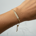 Gold-toned bar bracelet with sparkling pave crystals and adjustable slider chain, shown on a wrist with water droplets