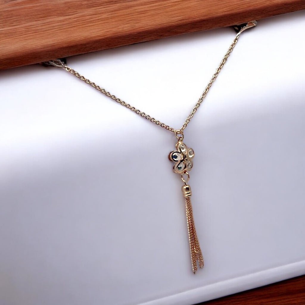 Gold floral tassel pendant necklace with crystal petals, worn on-model at the beach