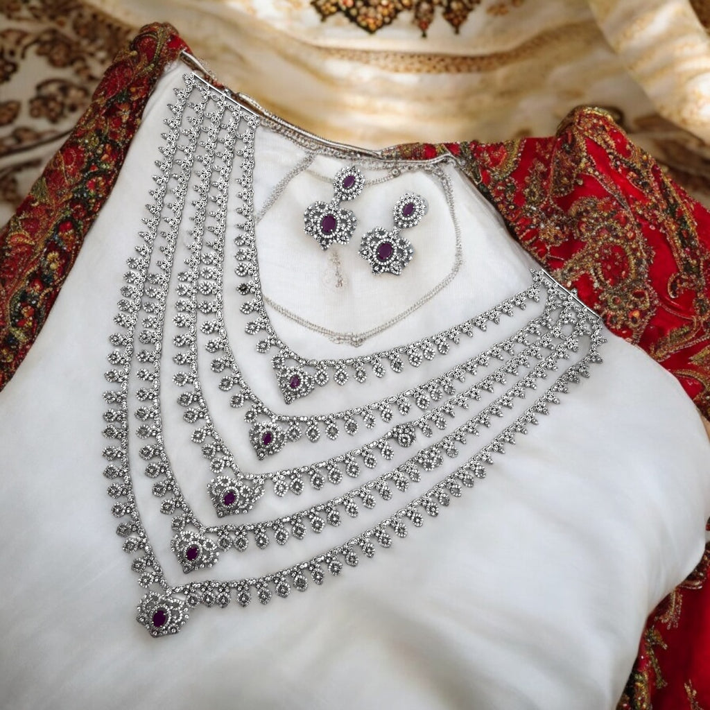 Silver-tone ruby & white stone multi-layered necklace set with matching earrings, flat-lay on bridal fabric