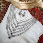 Silver-tone ruby & white stone multi-layered necklace set with matching earrings, flat-lay on bridal fabric