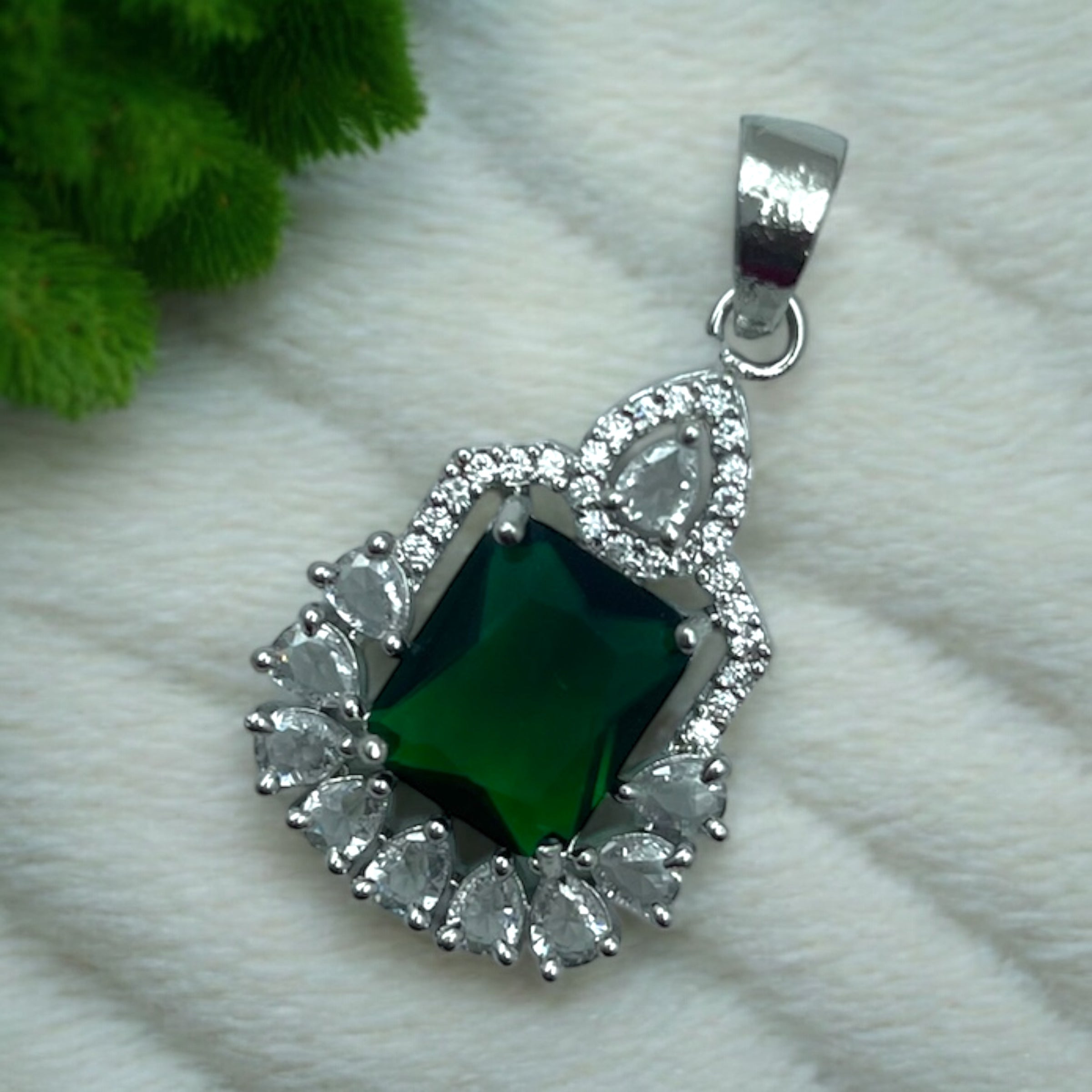 Silver-tone emerald-green halo pendant with pear-cut CZ accents, flat-lay close-up
