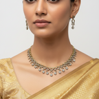 Gold necklace and earrings set with clear stones and floral drops, flat-lay on white cloth over autumn leaves