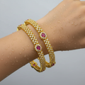 Gold-plated bangle set with crystal rows and oval ruby-red stones, worn stacked on wrist with water droplets