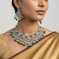 Kundan-style peacock necklace and chandelier earrings set with green stones and pearls, flat-lay on autumn leaves