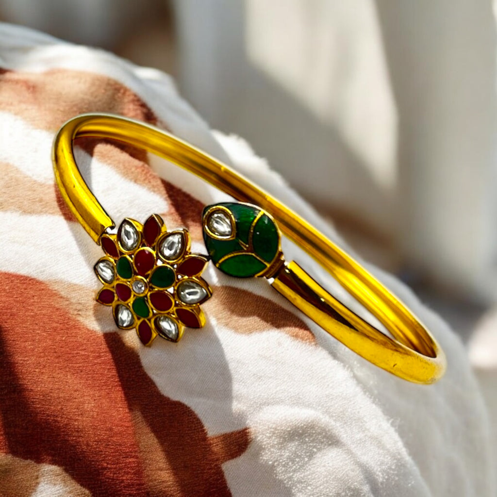 Gold-plated floral Kundan cuff bracelet with green leaf terminal, flat-lay close-up on fabric