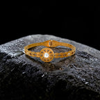 Gold bracelet with a central gemstone on a dark textured surface