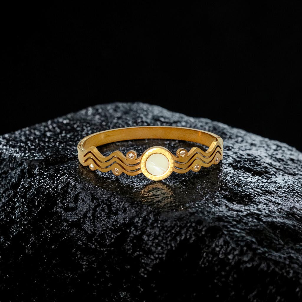 Gold bracelet with a wave design on a black textured surface