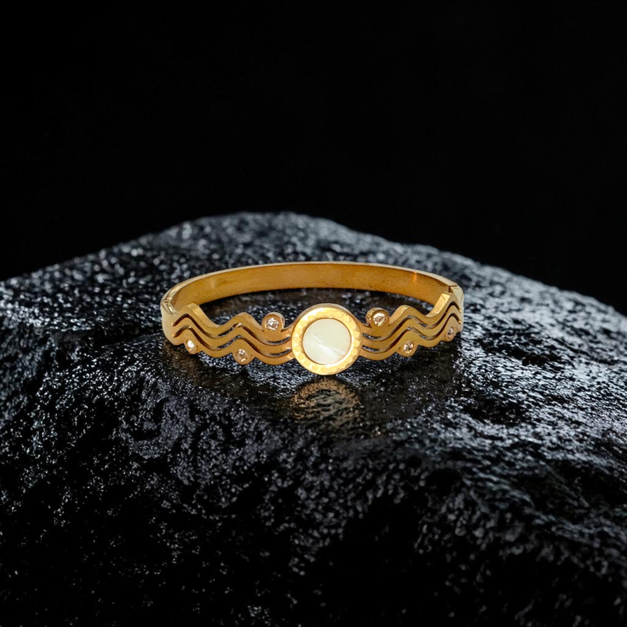 Gold bracelet with a wave design on a black textured surface