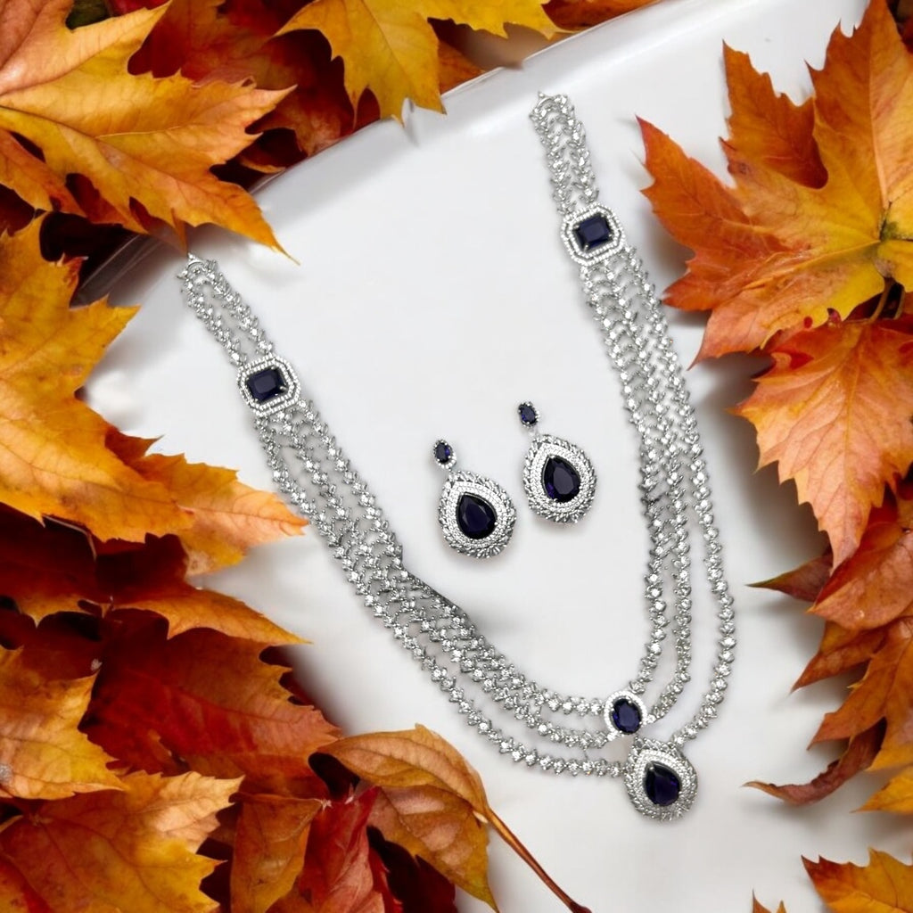 Silver-tone sapphire-blue necklace and drop earrings set, triple-layered crystal design, flat-lay with autumn leaves