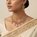 Woman wearing a gold necklace and earrings with a beige saree
