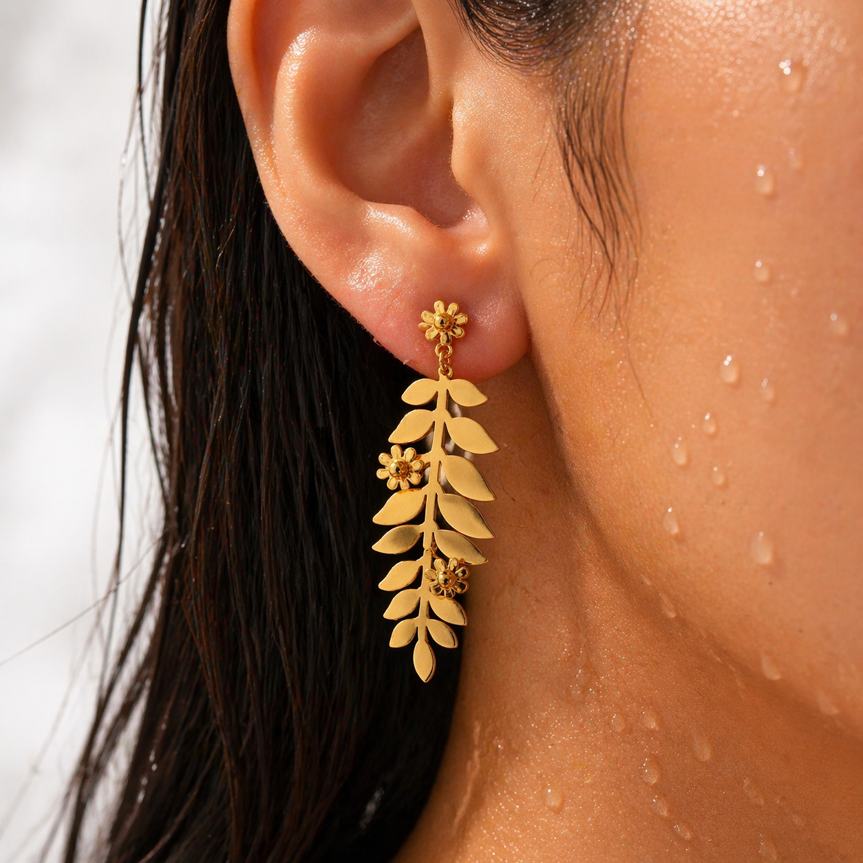 Close-up of a person wearing gold leaf earrings with a blurred background