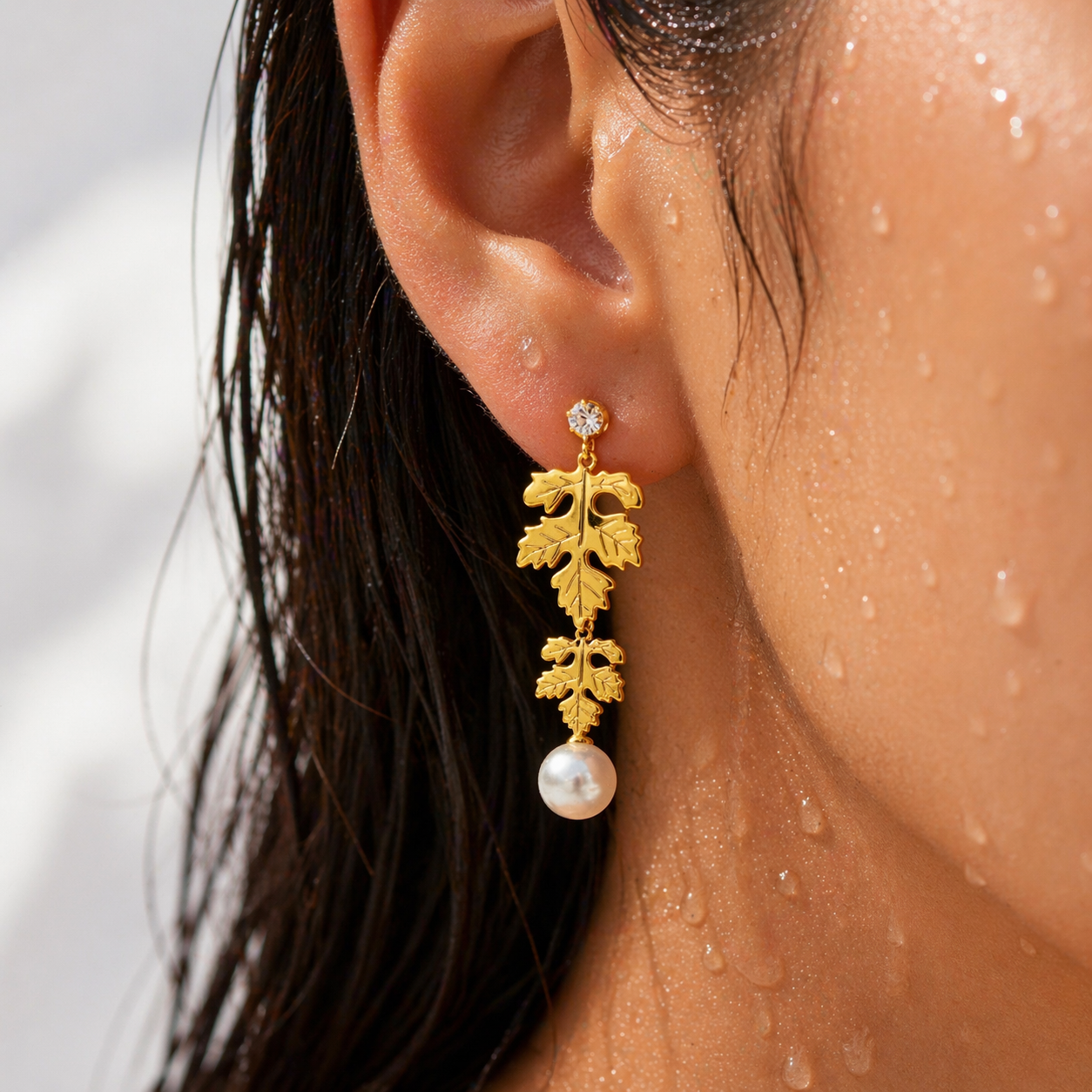 Close-up of a person wearing a gold leaf earring with a pearl drop.