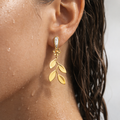 Golden  leaf earring worn by a person with a neutral background