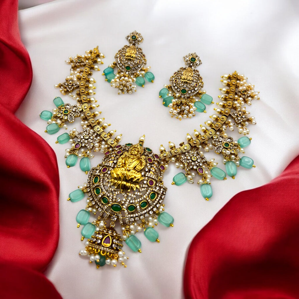 Gold Lakshmi temple necklace and earrings set with mint-green beads and pearls, flat-lay on red satin